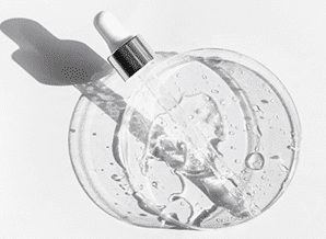 Transparent serum bottle with a dropper, casting a soft shadow, atop a smooth surface. Light reflecting off the liquid inside.