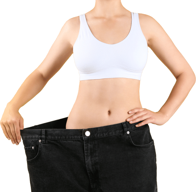 A woman in a white sports bra holds up oversized black jeans, showcasing her weight loss success with a confident smile.