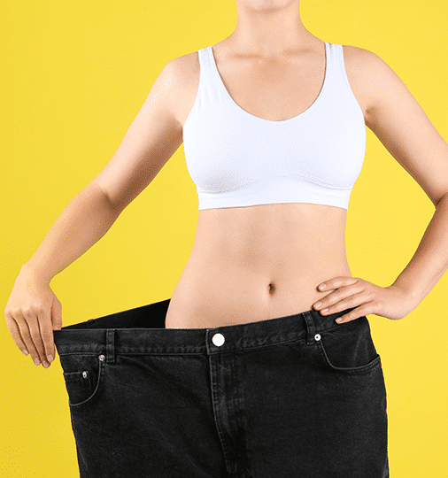 A woman in a white top and black jeans holds up a pair of large jeans