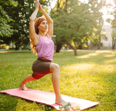A woman practicing yoga in a sunny park, surrounded by green grass and trees, focusing on her balance and posture.