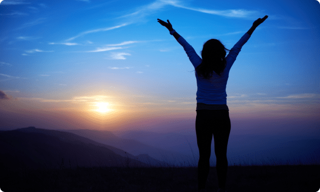 Silhouette of a woman with arms lifted high, enjoying a stunning sunset.