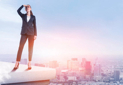 A woman in business attire stands on a ledge, gazing out over a sprawling cityscape.