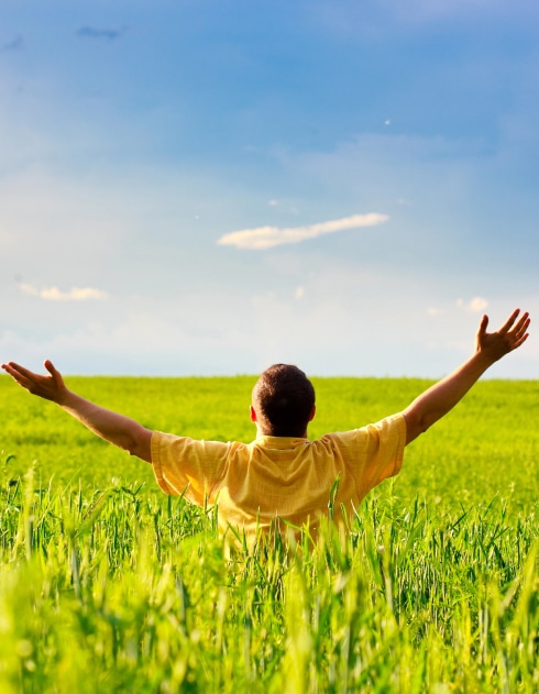 A man sits in a field, arms outstretched, enjoying the open space and nature around him.