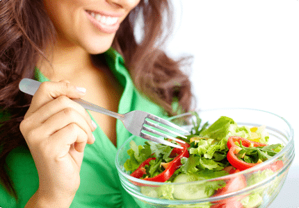 A woman with a fork in one hand and a bowl of colorful salad in the other, ready to eat.