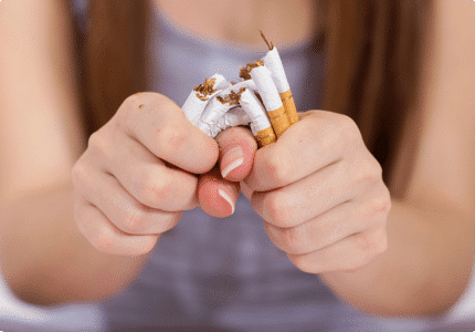 A person grips and crushes discarded cigarettes in their hands, symbolizing the act of quitting smoking.