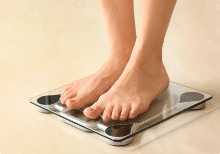 A person weighing themselves on a bathroom scale, glancing at the numbers with a thoughtful look.
