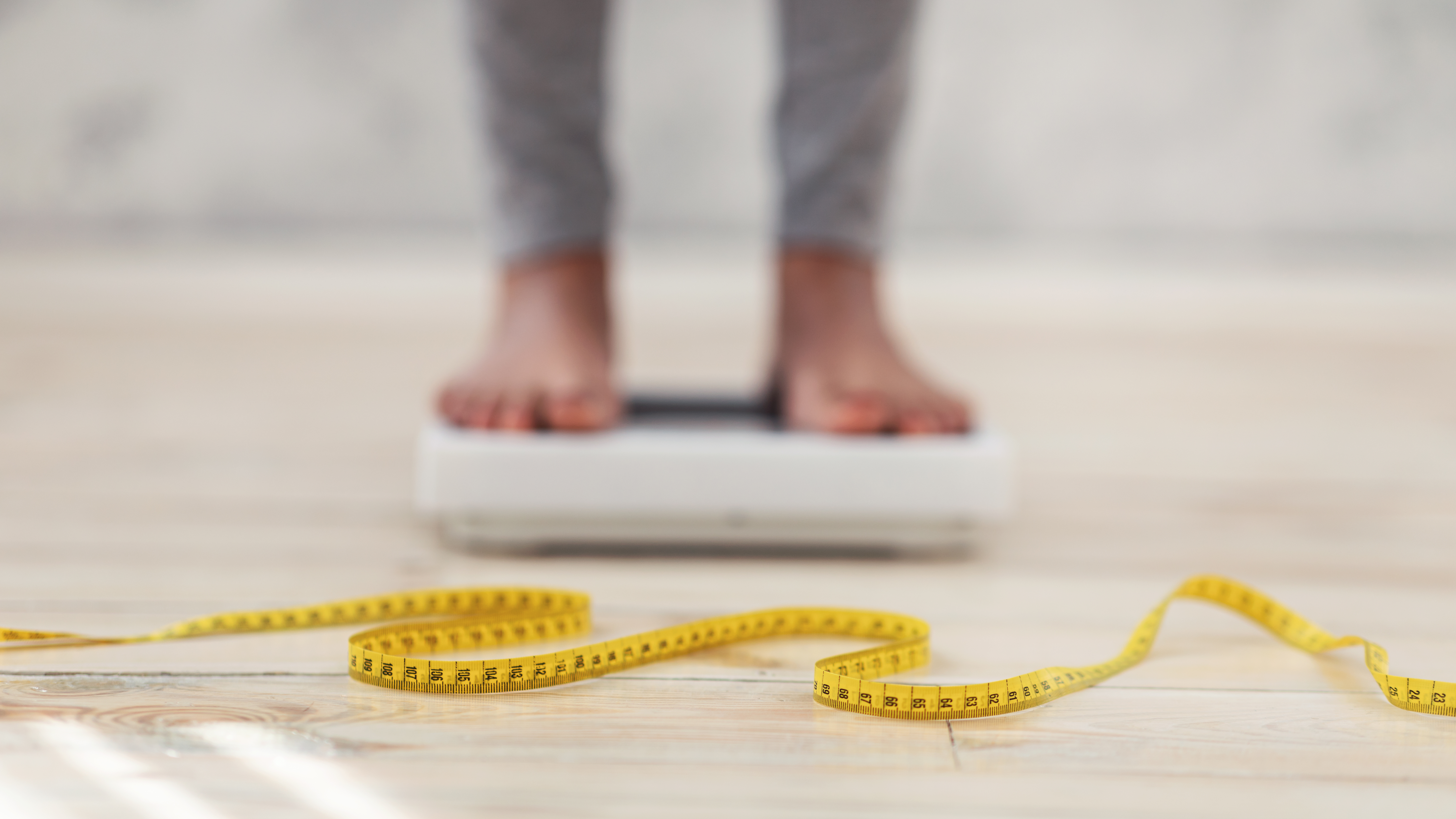 Unrecognizable black lady standing on scales, checking her weight, focus on measuring tape. Cropped view of African American woman fighting excess pounds, using slimming diet