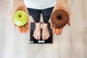 Diet. Woman Measuring Body Weight On Weighing Scale Holding Donut and apple. Sweets Are Unhealthy Junk Food. Dieting, Healthy Eating, Lifestyle. Weight Loss. Obesity