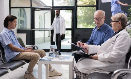Senior doctor standing beside elderly patient discussing health care treatment during checkup visit appointment in hospital waiting area. Old man filling insurance report before start consultation