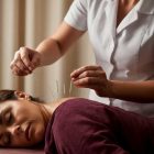 A professional administering acupuncture treatment on a patient lying on a treatment table in a calming, softly lit environment.