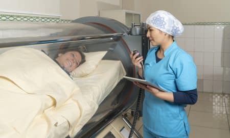 A nurse talking with a patient inside a cylindrical hyperbaric treatment machine