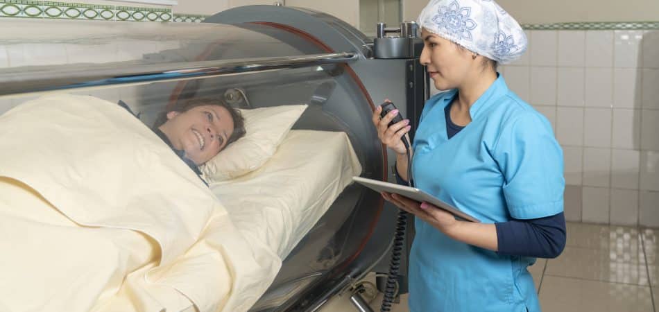 A nurse talking with a patient inside a cylindrical hyperbaric treatment machine