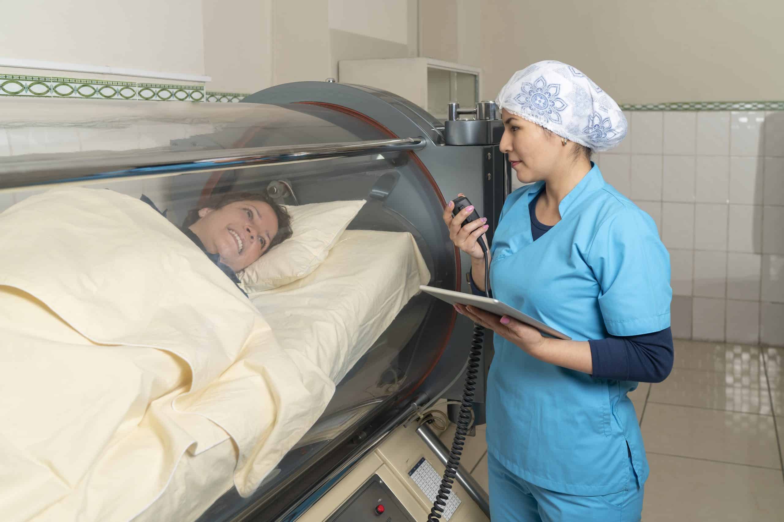 A nurse talking with a patient inside a cylindrical hyperbaric treatment machine
