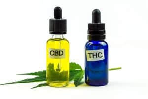 Two dropper bottles labeled "CBD" and "THC" sit next to a cannabis leaf on a white background, visually highlighting the CBD vs. THC comparison.