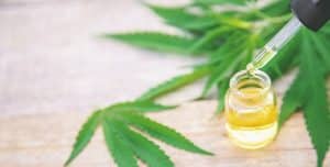 A glass dropper with yellow oil above a small bottle, featuring cannabis leaves in the background on a wooden surface, illustrates the difference between CBD vs. THC products.