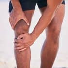 A person in athletic shorts holding their knee with both hands, possibly indicating knee pain or discomfort, standing outdoors—an image relevant to discussions about CBD vs. THC for managing joint issues.