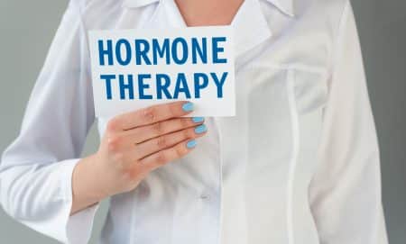 white coat doctor holding a card with "hormone therapy " written on it
