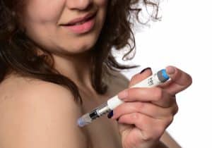 A person with curly hair uses a weight loss injection pen on their upper arm against a white background.