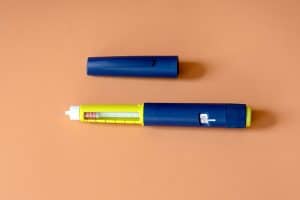 A blue and yellow Weight Loss Injection Pen with its cap removed, showing the dosage window and needle, is placed on a tan surface.